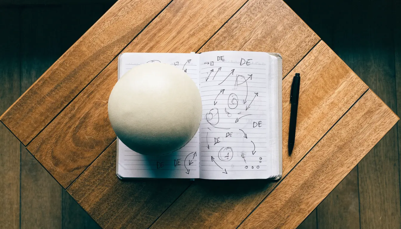 Ein Fußball liegt auf einem Notizbuch mit handgezeichneten Skizzen von Spielzügen, aufgenommen von oben auf einem Holztisch.
