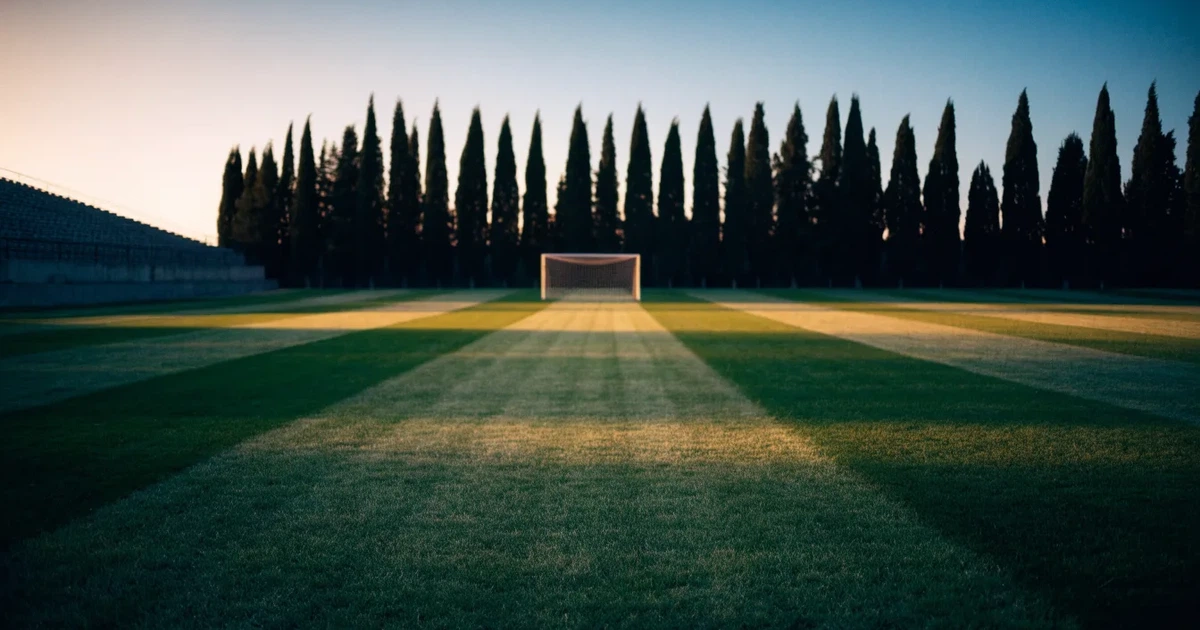 Ein Fußballtor mit Netz auf einem leeren Platz im Abendlicht, der Rasen frisch gemäht, im Hintergrund Zypressen.
