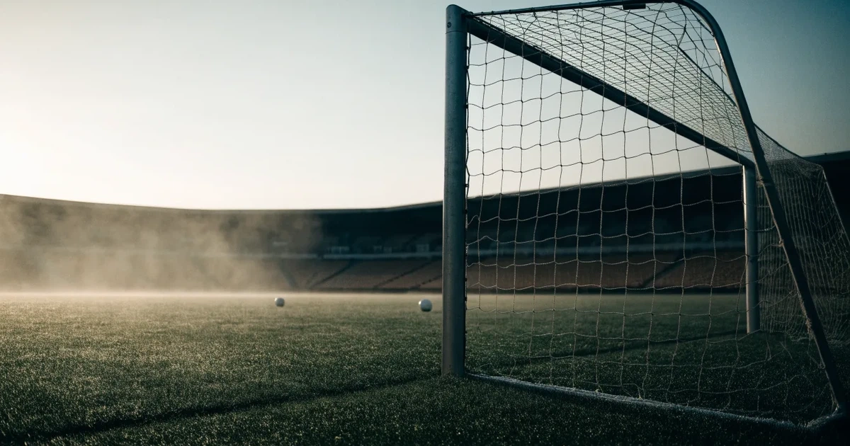 Ein Fußballtor mit Netz steht auf einem leeren Platz im Nebel der Morgendämmerung, der Rasen ist taufeucht.