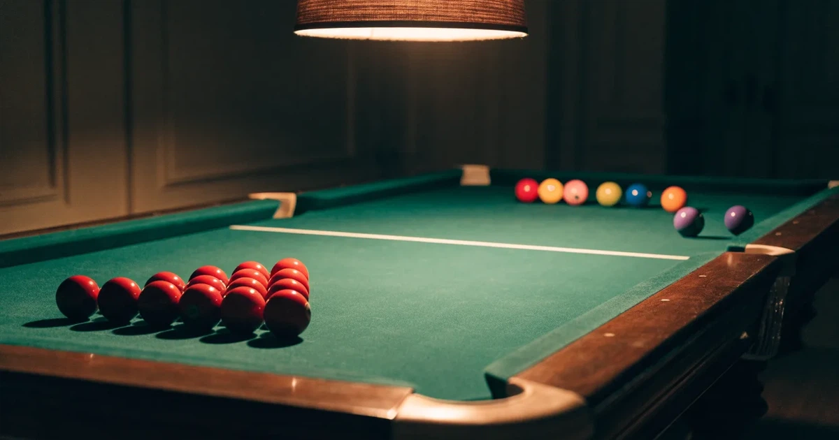 Ein Snookertisch mit grünem Tuch und aufgebauten roten Kugeln in einem abgedunkelten Raum unter einer hängenden Lampe.