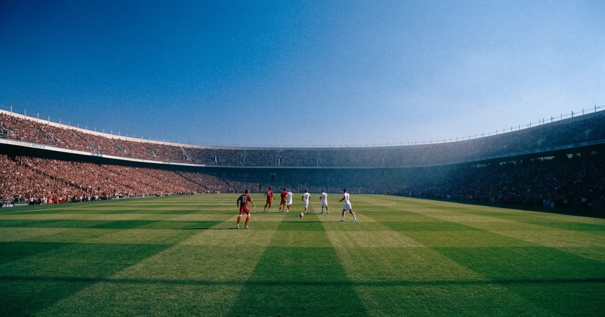 Ein Fußballstadion mit hellen Rängen unter strahlend blauem Himmel, davor ein sonnenbeschienener Rasen mit frisch gemähten Streifen.