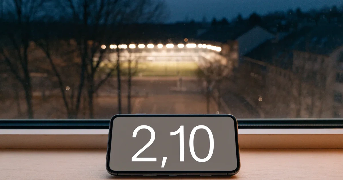 Ein hell erleuchtetes Stadion aus der Ferne bei Nacht, davor eine stille Straße und ein paar Bäume.