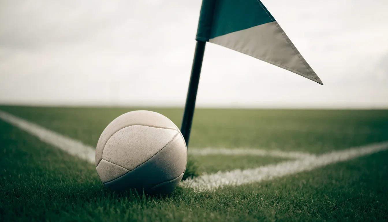 Ein Fußball liegt neben einer Eckfahne auf kurz gemähtem Rasen unter bewölktem Himmel.